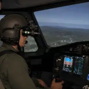 A helicopter pilot wears night vision goggles during an NVG online training simulation inside a modern cockpit