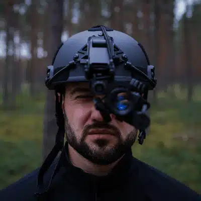 A man squints while using a gen 3 night vision monocular in a dense forest environment