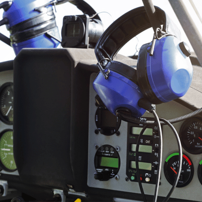 Blue aviation headset hangs over instrument panel, gauges and radios visible inside small aircraft cockpit
