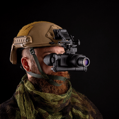 Soldier wearing helmet and monocular night-vision optic faces right against black studio background portrait photo