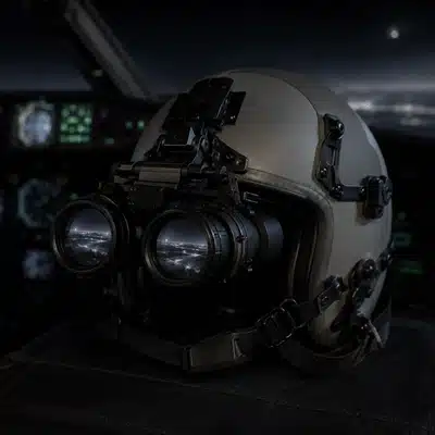 White phosphor night vision goggles are mounted on an aviation helmet inside a dim helicopter cockpit.