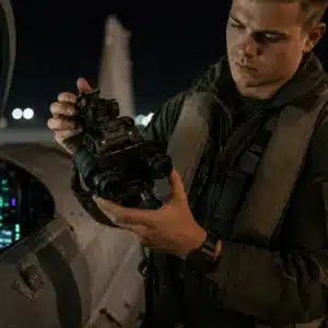 An aviation crew member examines gen 3 night vision goggles beside an aircraft cockpit during a nighttime equipment check