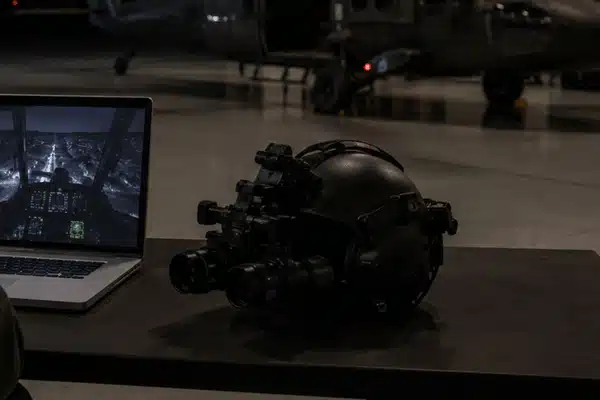 night vision goggle online training setup with a laptop, NVG helmet, and helicopter inside a dim aviation hangar
