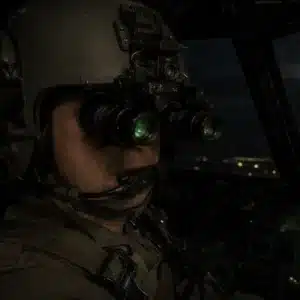 A close-up shows a helmeted pilot wearing aviation night vision goggles inside a dark cockpit, demonstrating how does night vision work for pilots in low-light conditions.