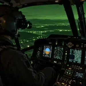 A pilot uses night vision goggles in a helicopter cockpit where nvis lighting keeps the instrument panel visible during nighttime flight