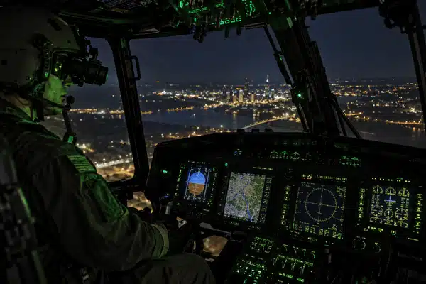 A helicopter pilot wearing night vision goggles flies over a city while nvis lighting illuminates the cockpit instruments and controls
