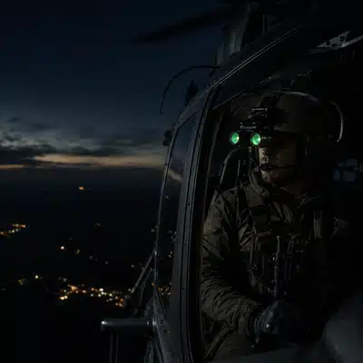 A pilot wearing night vision goggles sits inside a helicopter during an NVG training course at night