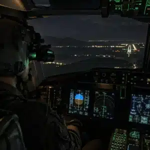 A pilot wearing night vision goggles operates an aircraft at night while approaching a lighted runway, illustrating ANVIS 10 aviation applications