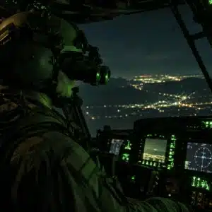 A helicopter pilot wearing night vision goggles operates the aircraft as nvis lighting softly illuminates the cockpit displays during a night mission