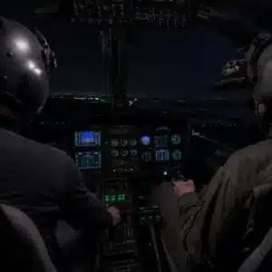 Two pilots wearing night vision equipment operate an aircraft together at night, showing how does night vision work during practical cockpit training.