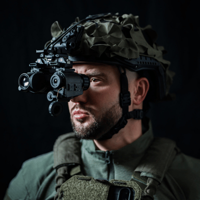 Soldier wearing helmet-mounted night vision goggles poses against dark background, demonstrating tactical equipment for training