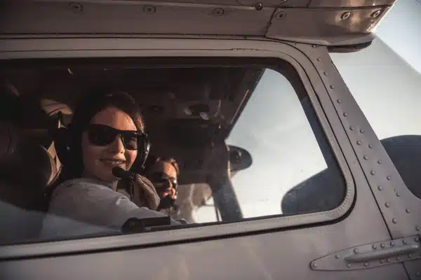 Smiling pilot wearing headset sits cockpit window seat, preparing flight with copilot beside during sunset