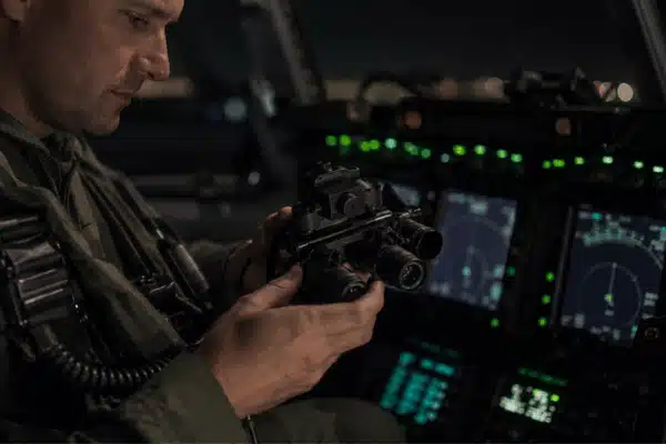 A pilot inspects gen 3 night vision goggles inside a dim aircraft cockpit before a nighttime flight