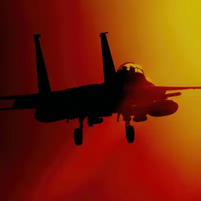 Silhouette of combat aircraft landing against fiery sky, landing gear down, evening training exercise underway
