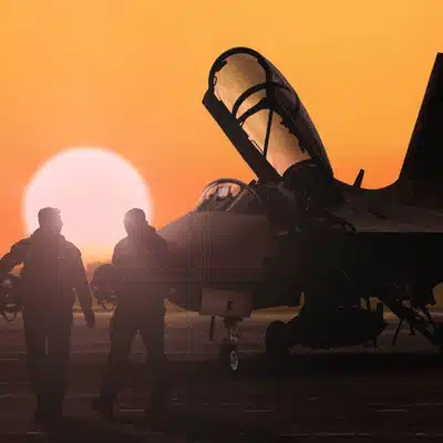 Silhouetted aircrew walk beside fighter jet at sunset, preparing for nvg white phosphor sortie today