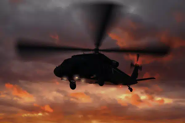 Military helicopter flying against dramatic sunset sky during evening mission with rotor blades spinning