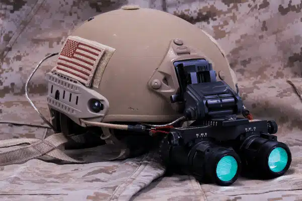 A military helmet with mounted gen 3 night vision goggles resting on camo fabric for operations