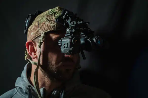 A soldier wears advanced night vision goggles attached to a camo helmet in low lighting
